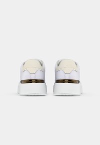 Sneaker bianche con talloni beige e suole spesse bianche, viste da dietro, con una striscia metallica con il marchio "Tommy Hilfiger".