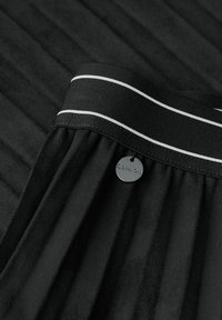 Gonna nera con design plissettato, texture liscia e vita nera con strisce bianche. Include un'etichetta metallica rotonda.