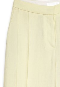 Pantalons jaune clair en tissu texturé, avec des plis marqués, une taille lisse et des poches latérales pour la fonctionnalité.