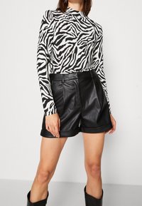 Svart och vit zebrarandig långärmad topp som kombineras med högmidjade svart faux läder shorts, med uppvikta  ärmar och framfickor.