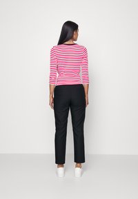 Red and white striped top with three-quarter sleeves, paired with black pants and white sneakers. Simple, fitted design, minimal accents.