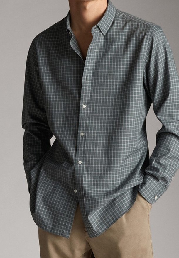 Camicia a maniche lunghe con bottoni di colore verde scuro, caratterizzata da un motivo a griglia in tonalità più chiare. Realizzata in tessuto morbido con colletto classico e orlo dritto.