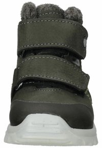Zapato de cuero verde con dos correas de Velcro, acentos de piel de oveja gris, puntera redondeada y suela de goma blanca. Presenta costuras y superficies texturizadas.