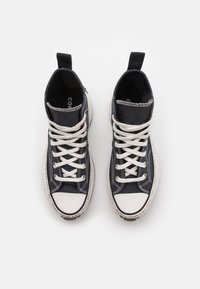 Para czarnych sneakersów typu high-top z białymi sznurowadłami i czubkami, widocznych z góry na białym tle.