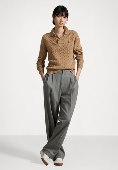 Tan cable knit sweater with a collared neck and a single button, paired with wide-leg gray trousers and white sneakers.