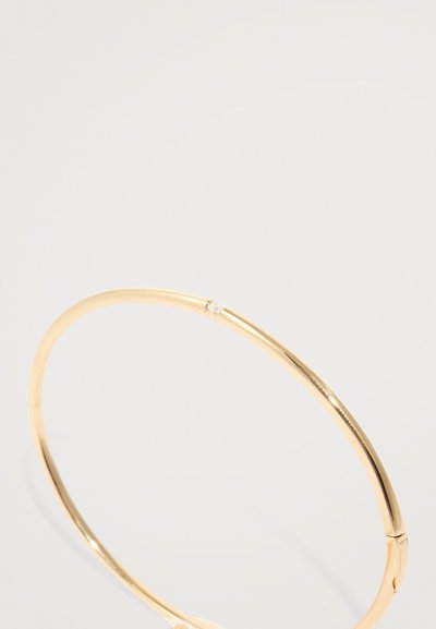 Bracciale in oro con una forma liscia e arrotondata, adornato con un piccolo cristallo trasparente vicino alla chiusura, caratterizzato da una finitura lucida.