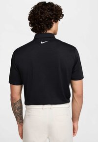 Melnā polo krekla ar īsām piedurknēm, ar strukturētu audumu un baltu Nike logo mugurā. Kombinēts ar gaišiem biksēm.