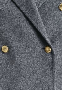 Grijze wollen jas met een gestructureerde afwerking, voorzien van een dubbelknops ontwerp en gouden knopen met een reliëf logo detail.