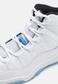 Baltas sportinis batelis su tekstūruotu paviršiumi ir mėlynomis detalėmis, plokščiomis raištelėmis ir skaidriu guminiu padu. Stilingas dizainas ir matomi sutvirtinimai.