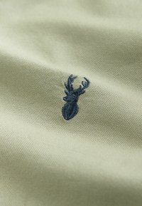 Beige-kangasta, jossa on kiinteä kudos, ja pinnalla on tummansininen brodeerattu peuranpääkuvio.