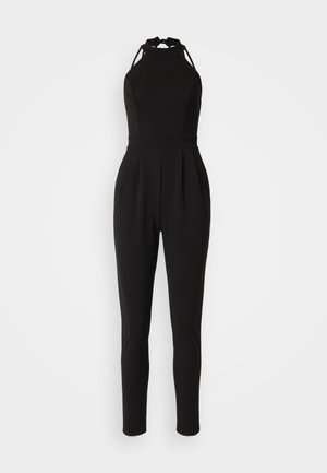 Schwarzer Jumpsuit mit einem Halsband-Design, tailliertem Oberteil und verjüngten Beinen. Verfügt über Ausschnitte an den Schultern und Falten in der Taille.