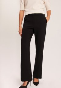 Czarne, dopasowane spodnie o prostym kroju, z gładką fakturą i bocznymi kieszeniami. W komplecie z jasnym topem i czarnymi szpilkami.