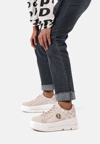 Sneakers platform rosa chiaro con lati a fantasia, design con lacci e suole spesse bianche, abbinati a jeans in denim scuro.