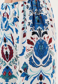 Bloemmotief stof met levendige blauwe, rode en teal ontwerpen op een witte achtergrond. Heeft een geraffineerde taille en een lichte textuur.
