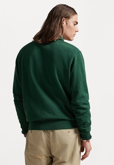 Sweat-shirt vert à col rond, avec des poignets et un ourlet côtelés, une texture douce et une coupe décontractée, associé à un pantalon beige.