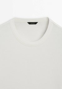 T-shirt blanc à col rond posé à plat montrant l'encolure et le haut de la poitrine avec une petite étiquette noire à l'intérieur du col.