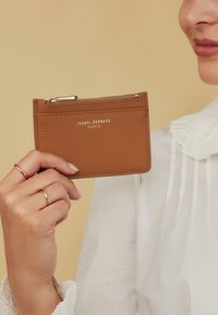 Brown leather card holder with zip pocket; embossed brand name "ISABEL BERNARD PARIS" in gold; smooth texture; minimalistic design.