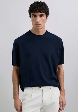 Camiseta de manga corta azul marino, escote redondo, tejido suave, corte holgado, combinada con pantalones de color claro, diseño minimalista sin patrones.