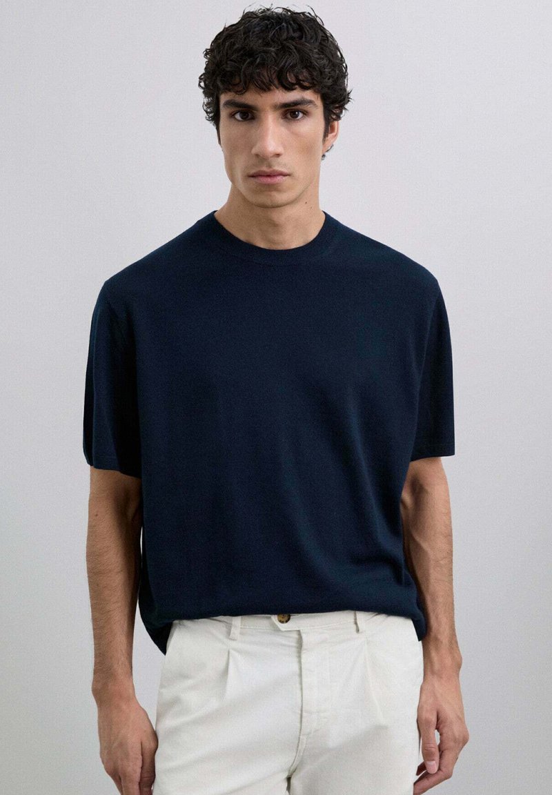 Camiseta de manga corta azul marino, escote redondo, tejido suave, corte holgado, combinada con pantalones de color claro, diseño minimalista sin patrones.