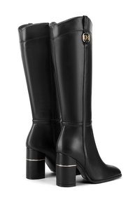 Stivali alti in pelle nera con design strutturato, punta quadrata e tacchi a blocco lucidi con una fascia d'accento dorata. Chiusura laterale con zip visibile.