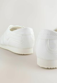 Hvide sneakers med et struktureret, slangelignende mønster. Rund form, blødt materiale og en flad sål med subtile riller.