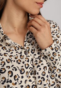 Blouse imprimée léopard en tissu léger, avec une fermeture à boutons, un col et des couleurs contrastantes noir, marron et crème.