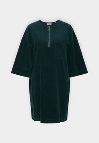 Overmaatse donkergroene corduroy jurk met een ronde hals, korte mouwen, een kwart-rits aan de voorkant en een zak op de linkerkant van de borst.