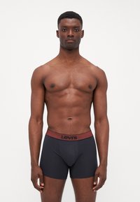 Svarta boxerkalsonger i ett slätt tyg, med en mörkröd midja som har Levi's-logotypen i svart. Enkelt mönster, åtsittande form.