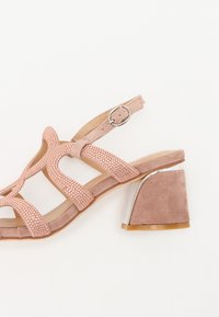 Rosa semskede høyhælte sandaler med stropp og spenne, med kryssremmer pyntet med små rhinestones og en sølvdetalj på hælen.