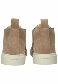 Botas de tobillo de ante color beige con acabado suave, suela de goma blanca y lengüetas en la parte trasera. Inscripción "BLACKSTONE" en el talón.