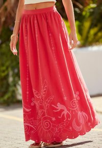 Jupe longue et fluide en tissu corail avec des motifs brodés blancs, comprenant des feuilles, un singe et des tourbillons. Taille élastique, ourlet festonné.