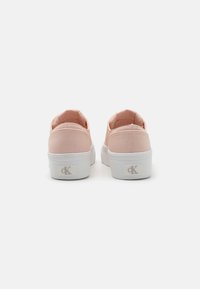 Pink canvas slip-on shoes with white rubber soles, featuring a logo on the heel and textured fabric for grip and style.