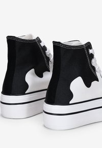 Zapatillas altas con una combinación de colores blanco y negro; lona texturizada, costuras en contraste y un diseño lateral con patrón. Suela blanca con acentos en negro.