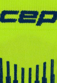 Primo piano di un tessuto di maglia verde con testo blu scuro e motivi a righe verticali intrecciati nel materiale.