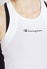 Vit och svart atletisk linne med en slim design. Har en svart "Champion"-logotyp på framsidan och kontrasterande axelband.