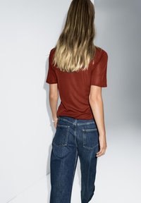 Rotes T-Shirt mit kurzen Ärmeln, kombiniert mit locker sitzenden, dunkelblauen Jeans aus Denim, die einen geraden Schnitt und sichtbare Gesäßtaschen aufweisen.