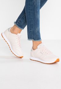 Ljust rosa sneakers med en slät läderöverdel, tygdetaljer, en vit mellansula och en texturerad brun gummisula, med en snörningsdesign.