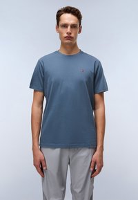 T-shirt en coton bleu avec un col rond, des manches courtes et un petit logo rouge et blanc sur la poitrine. Coupe décontractée, texture uniforme.