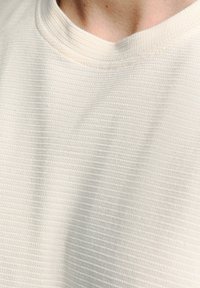 Crème-kleurige textielstof met een ribbelontwerp en een ronde halslijn. Nadruk op het subtiele patroon en de zachte textuur.