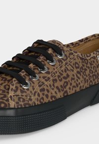 Χαμηλό sneaker με καφέ και μαύρο ύφασμα με λεοπάρ μοτίβο, μαύρα κορδόνια, ασημένιες μπότες και παχιά μαύρη υφασμάτινη καουτσούκ σόλα.