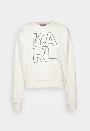 Bílá mikina s dlouhým rukávem s černými obrysy písmen tvořících slovo „KARL“ a siluetou v bočním profilu začleněnou do písmene „K“.