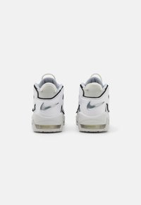 Nike-sneakers met een bovenwerk van wit leer, zwarte accenten, zilveren swoosh en zichtbare luchtkussens. De achterkant toont een gevoerde kraag en een treklip.