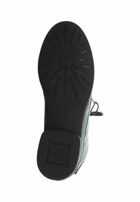 Suola in gomma nera con un motivo di grip texture che presenta frecce e un emblema circolare. Lato in pelle con un piccolo dettaglio di lacci rossi.