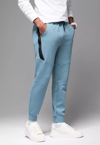 Jasnoniebieskie spodnie dresowe z czarnymi akcentami po bokach, ściągaczami na końcach nogawek i kieszeniami. Wykonane z miękkiego materiału, charakteryzujące się luźnym krojem i elastycznym pasem ze sznurkiem.