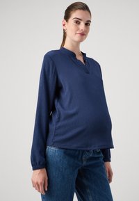 Marine blå langermet topp med teksturert design, utstyrt med halvspalte hals og elastiske mansjetter, kombinert med blå jeans.