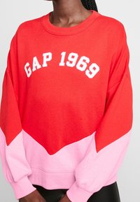 Felpa color block rosso e rosa con la scritta "GAP 1969" in bianco sul petto, collo tondo e maniche rilassate.
