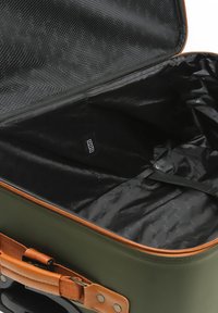 Valigia rigida verde con accenti beige, dotata di apertura con zip, interno nero e tasca in rete per una sistemazione organizzata.