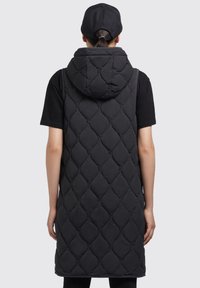 Black quilted long vest with a hood, featuring a diamond pattern and elastic detailing. Worn over a short-sleeve shirt, black leggings visible.