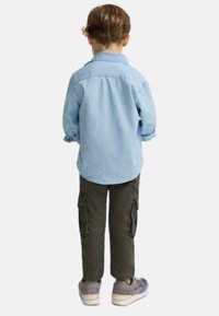 Camisa de botones azul claro, pantalones cargo verdes con bolsillos laterales, zapatillas gris con suelas blancas, vista desde la parte trasera.