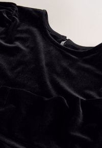 Schwarzes Samtkleidungsstück mit einer weichen, glatten Textur, ausgestattet mit einem runden Ausschnitt und einem kleinen Reißverschluss am Rücken.